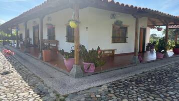 A building with a tiled roof, a porch with potted plants, and a stone-paved ground.