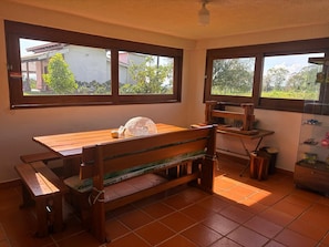A room with a wooden bench, a small table, and a shelf with items. There are windows providing a view of greenery outside. - Vrbo Property (rural)