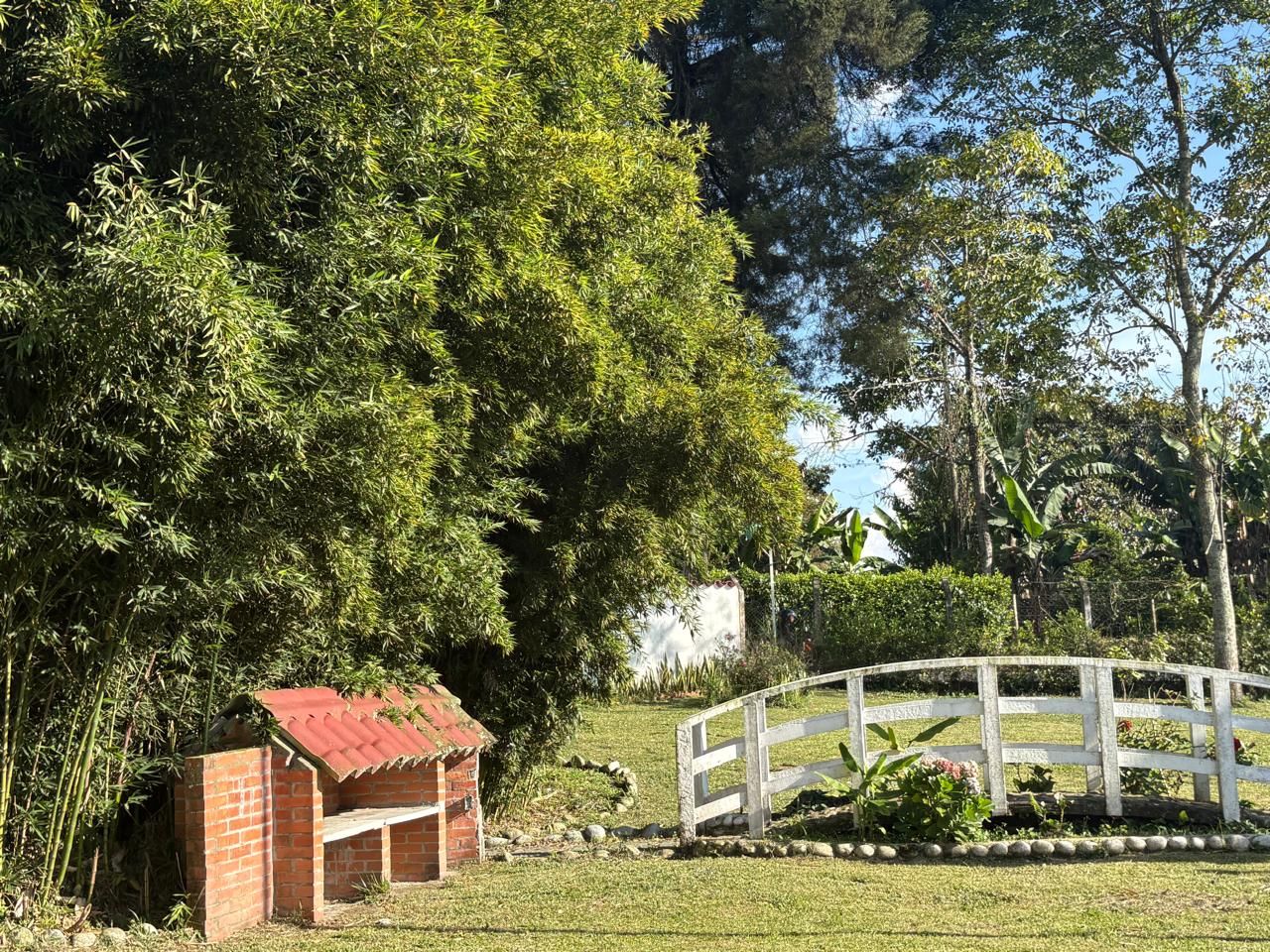A brick structure with a red roof, a white fence, and a grassy area with trees.
