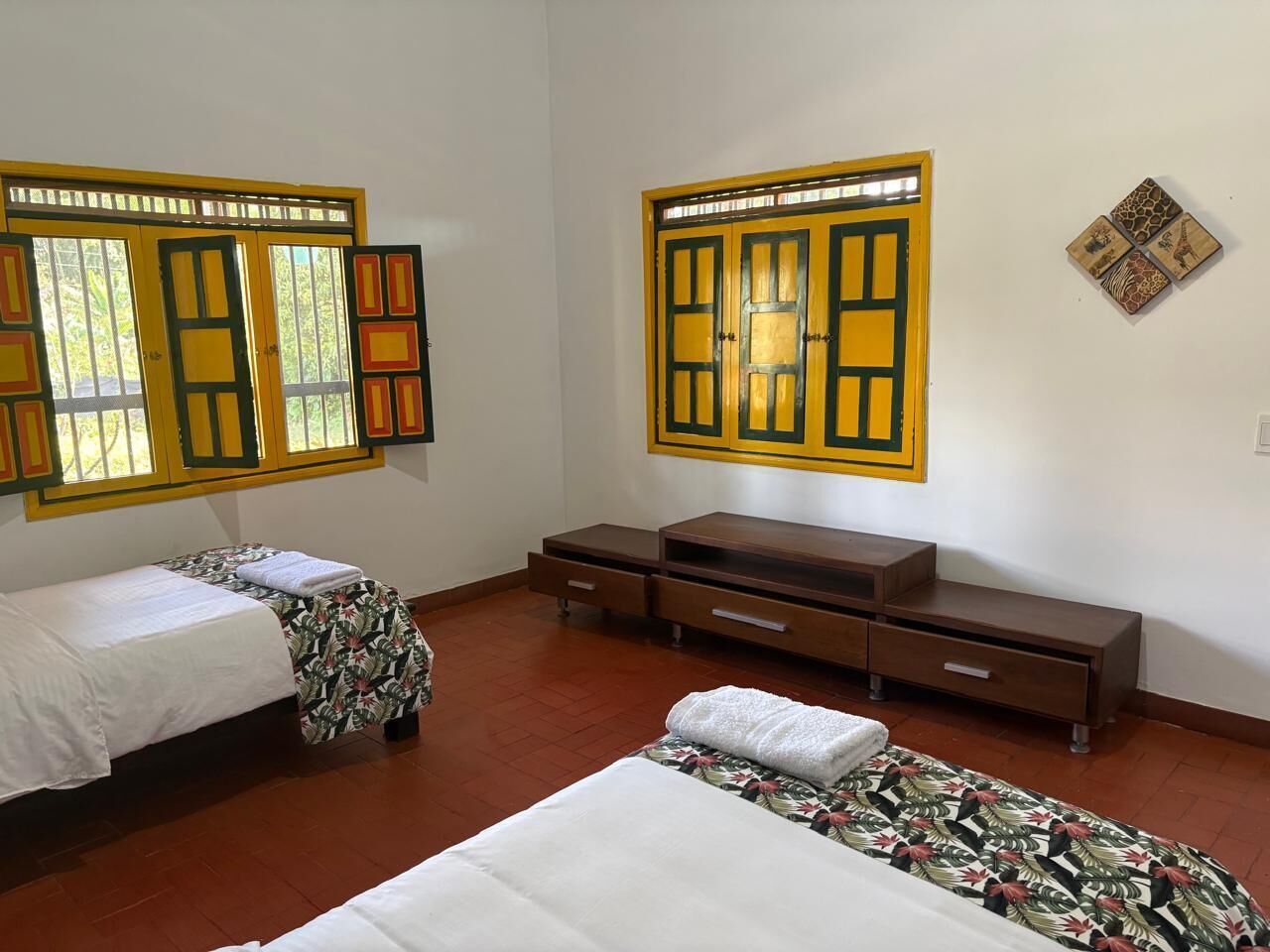 A room with two beds, a wooden dresser, and a wall-mounted television.