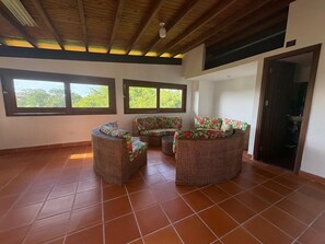 A spacious room with a high ceiling and large windows, furnished with wicker furniture and a tiled floor. - Coffee farm 15 minutes from the coffee park (rural)