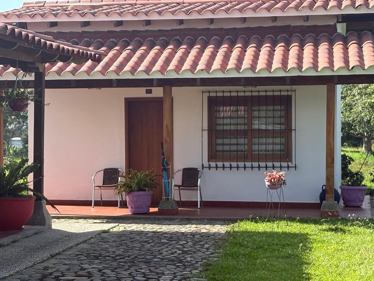 A covered porch with a tiled roof, two chairs, a potted plant, and a window with bars.