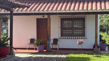 A covered porch with a tiled roof, two chairs, a potted plant, and a window with bars.