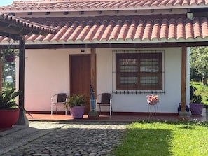 A covered porch with a tiled roof, two chairs, a potted plant, and a window with bars. - Coffee farm 15 minutes from the coffee park (rural)