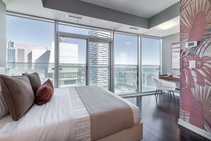 Ein modernes Schlafzimmer mit einem großen Bett, einem Schreibtisch und Blick auf die Stadt durch raumhohe Fenster.