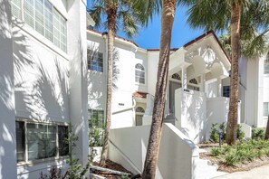 A white building with a covered outdoor area, palm trees, and a staircase. - Luxury Golf Cart & View, Steps to Beach,Pool,Tram (Miramar Beach)