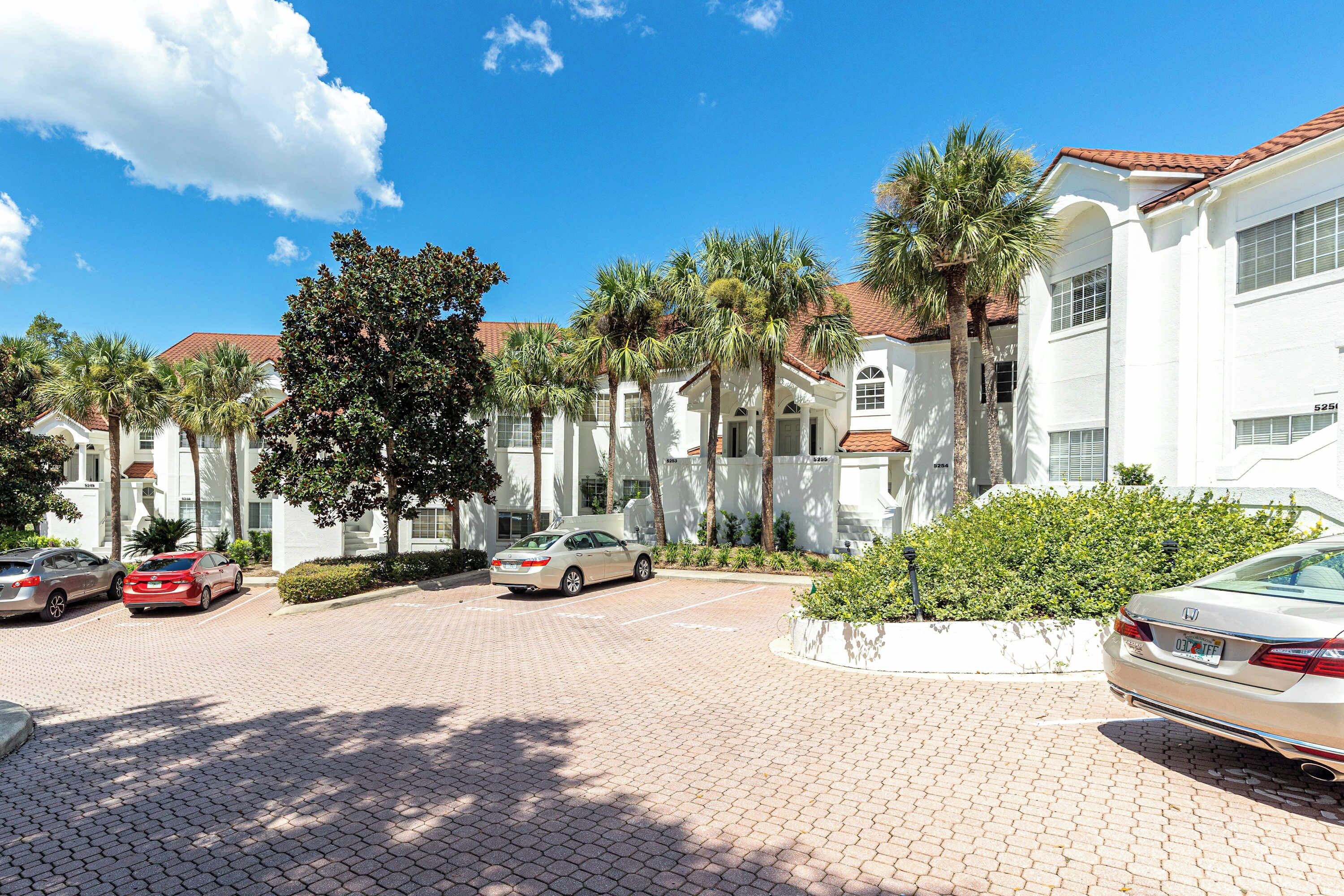 A residential area with white buildings, palm trees, and parked cars.