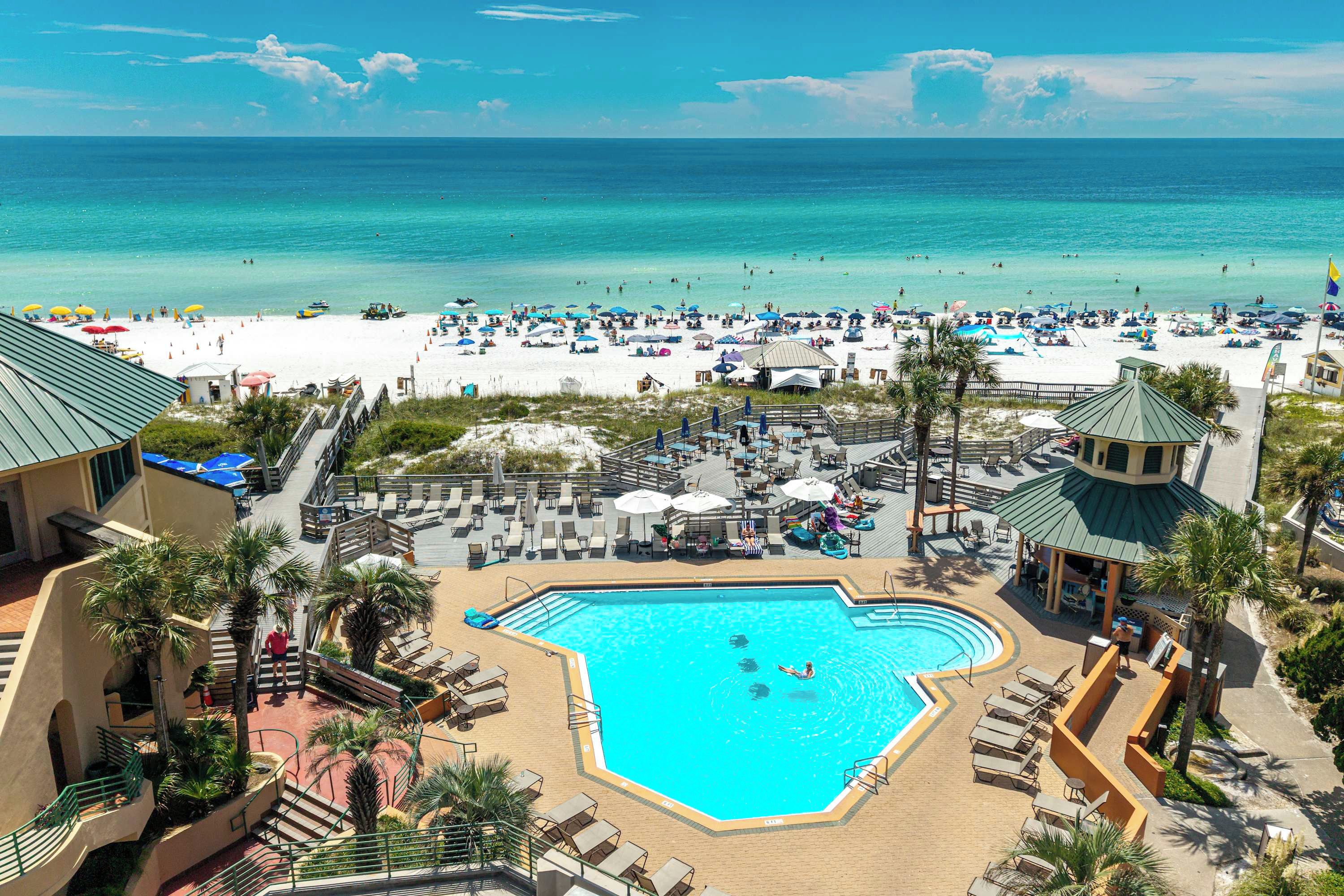 A resort with a central swimming pool, beach area, and a view of the ocean.