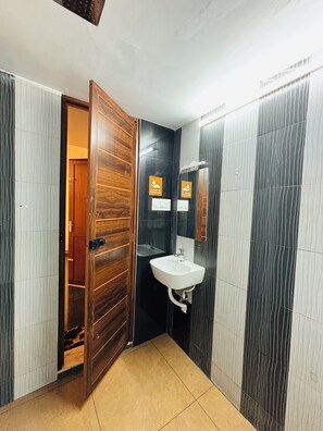 A bathroom with a wooden door, a white sink, and a mirror. - Fort Grande ONE (Kochi)