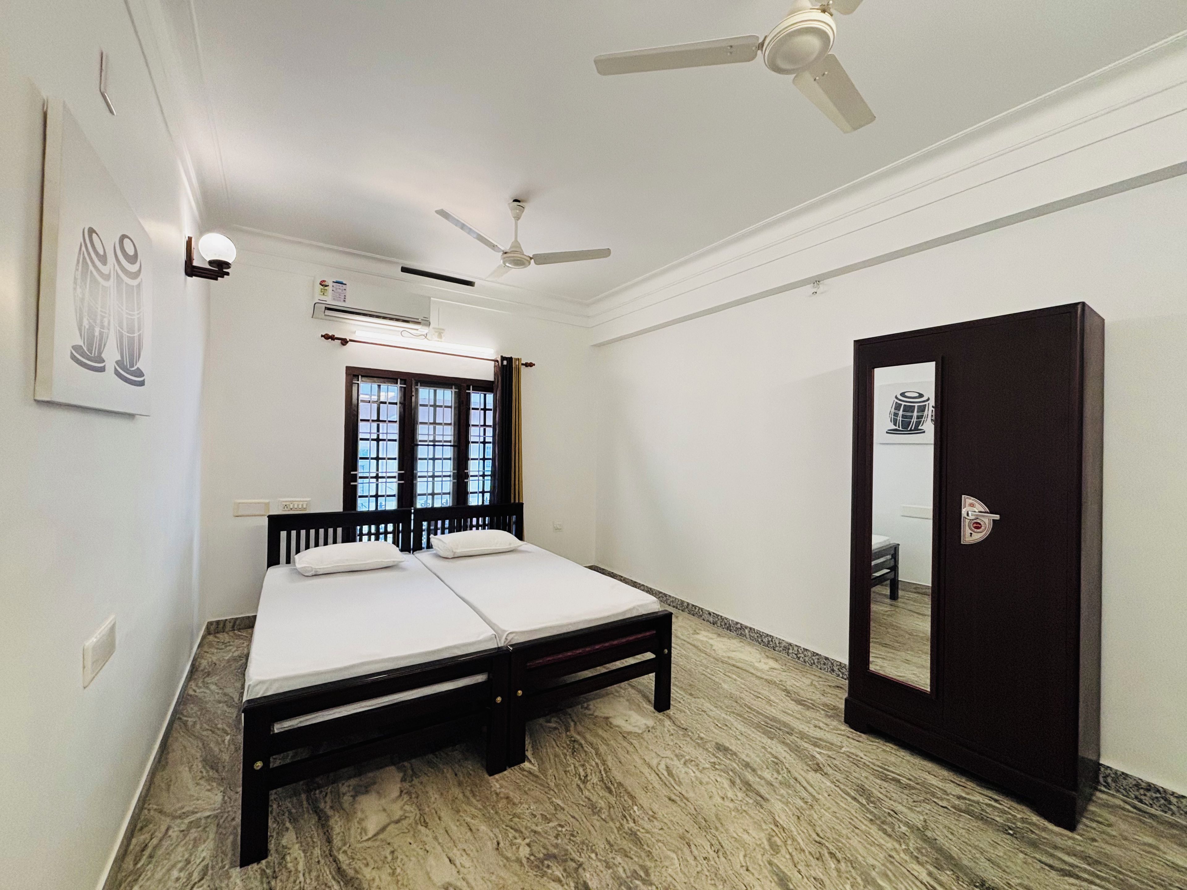 Una habitación con cama, ventilador de techo, ventana con cortinas y puerta con cerradura.