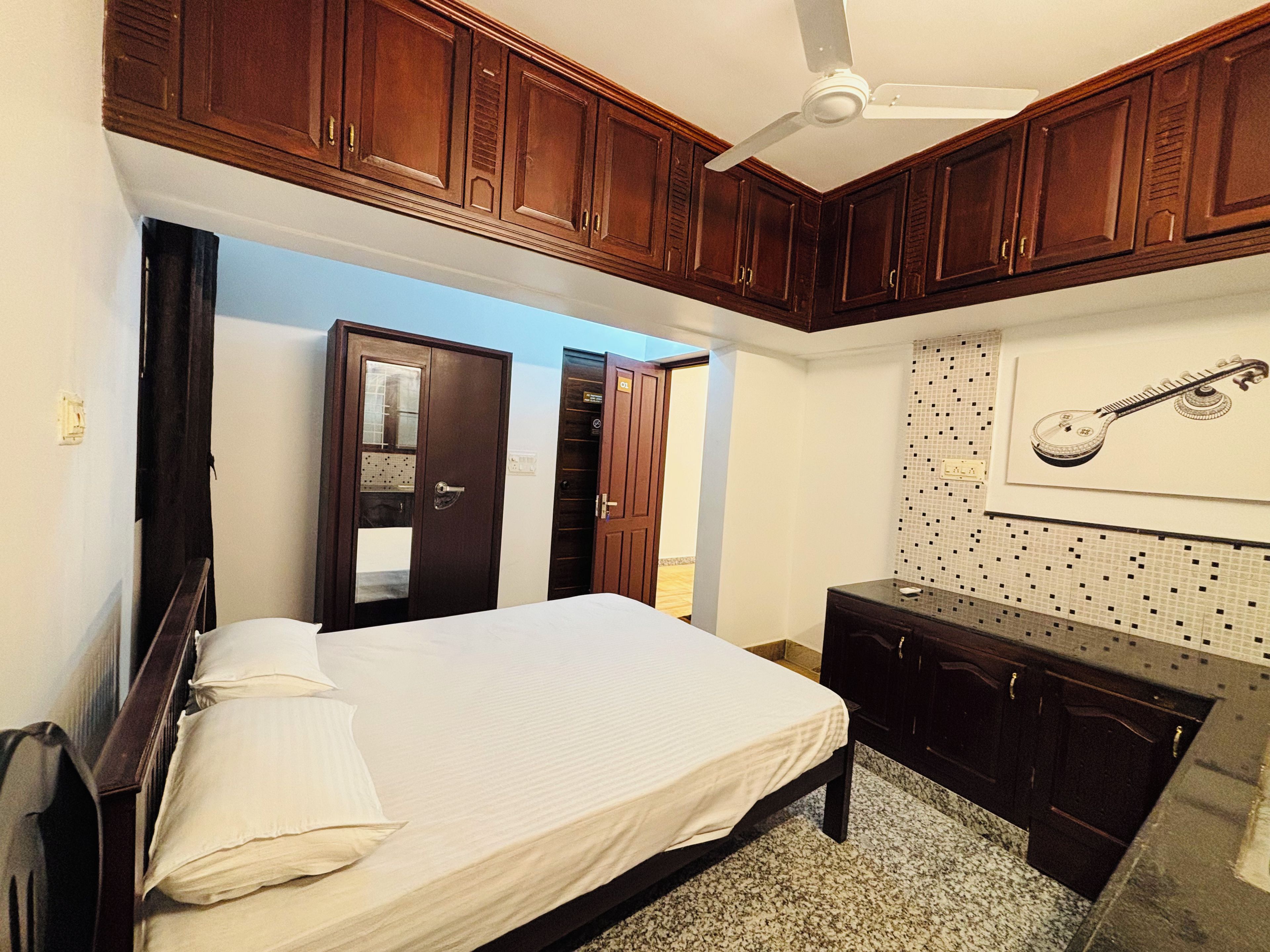 A bedroom with a bed, wooden cabinets, a ceiling fan, and a wall-mounted guitar.