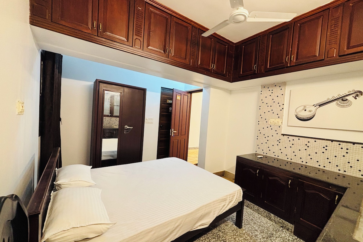 A bedroom with a bed, wooden cabinets, a ceiling fan, and a wall-mounted guitar.
