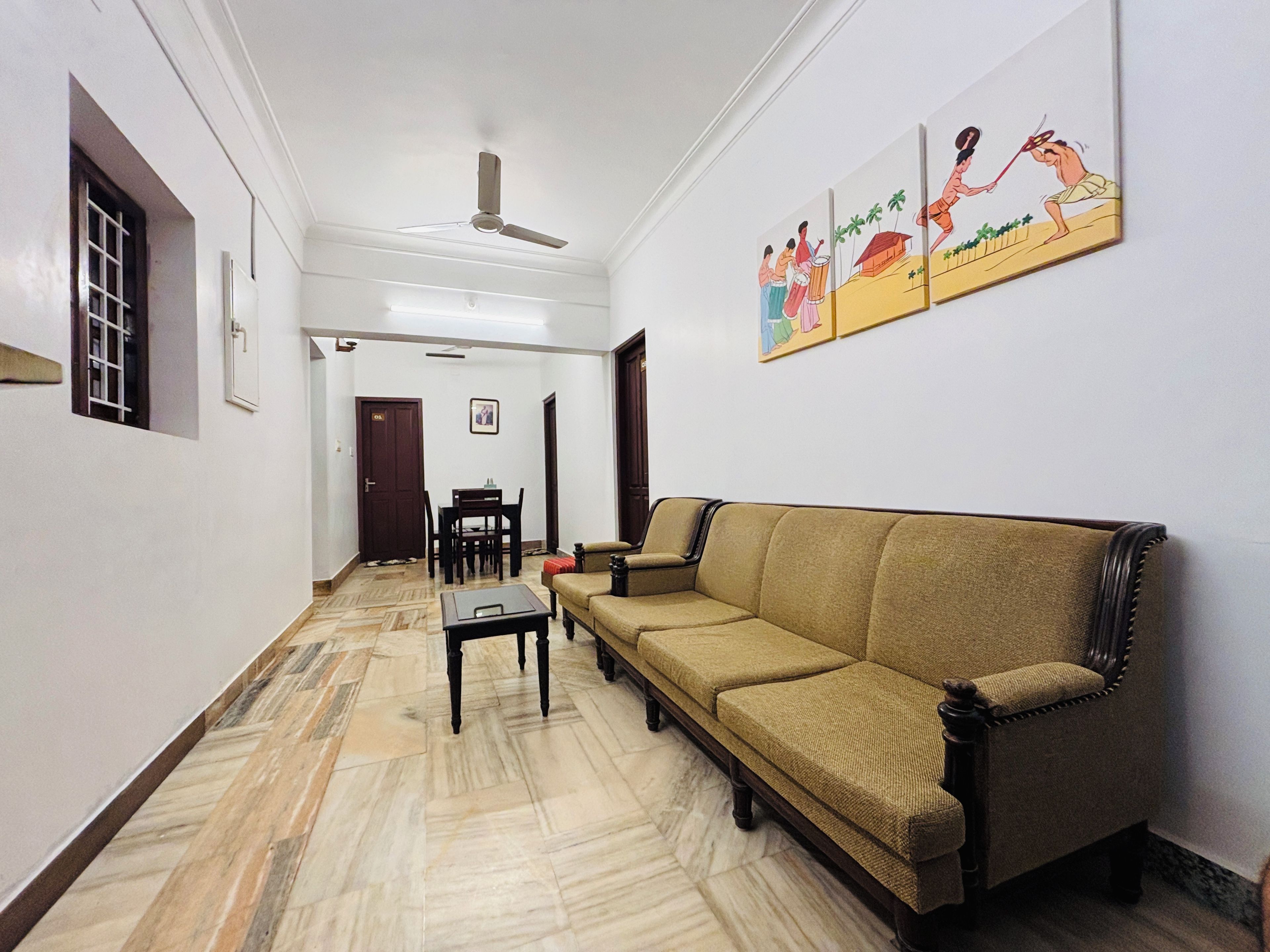 Una sala de estar con sofá, una mesa de comedor y sillas. Hay un ventilador de techo y una puerta que da a otra habitación.