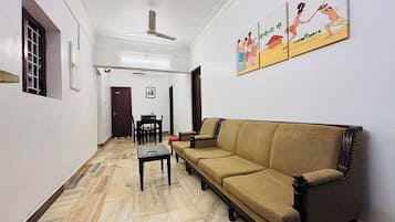 Una sala de estar con sofá, una mesa de comedor y sillas. Hay un ventilador de techo y una puerta que da a otra habitación.