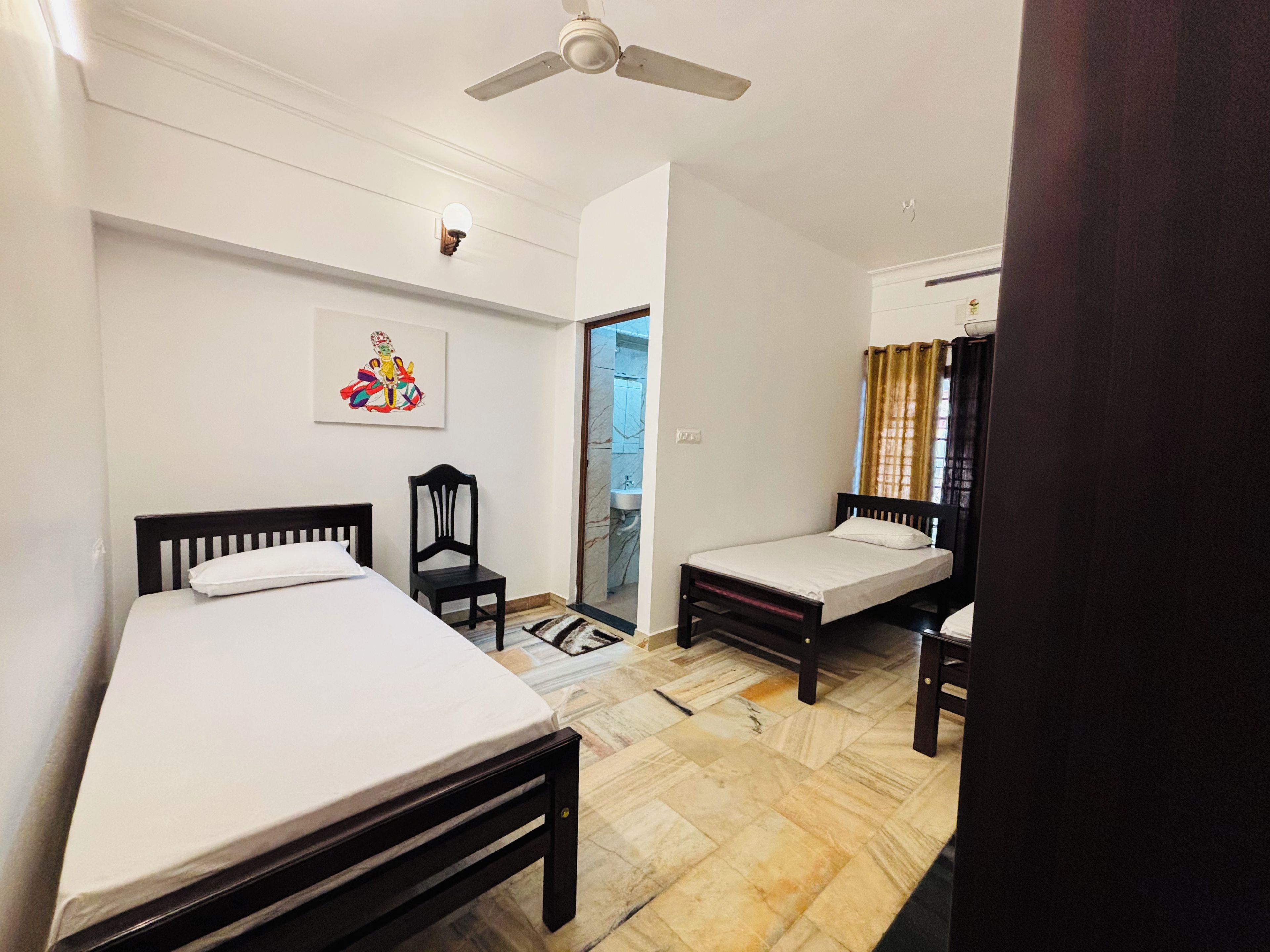 A room with two single beds, a ceiling fan, a wall-mounted light, and a door leading to a bathroom.