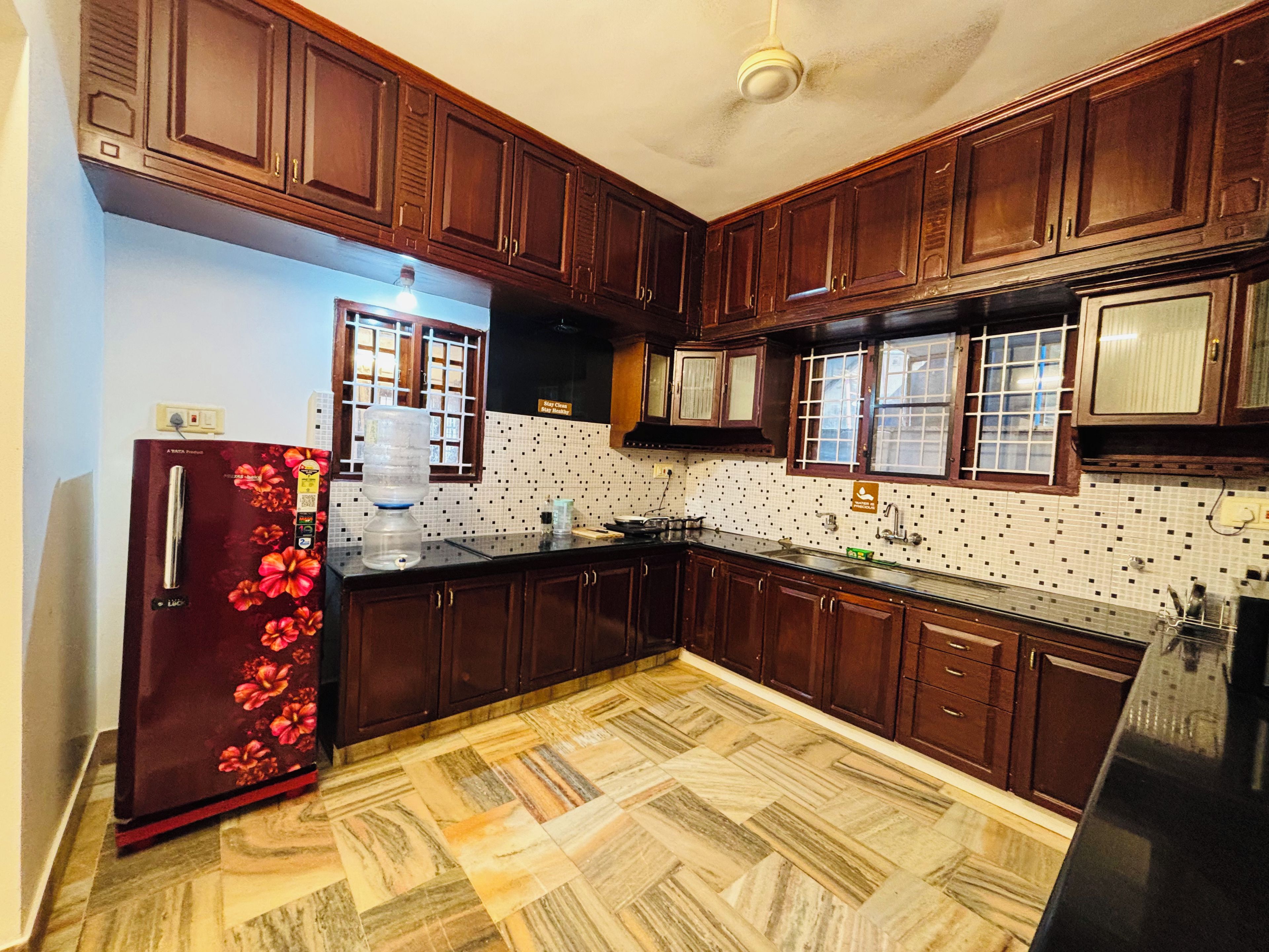 A kitchen with wooden cabinets, a refrigerator, a water dispenser, and a tiled backsplash.
