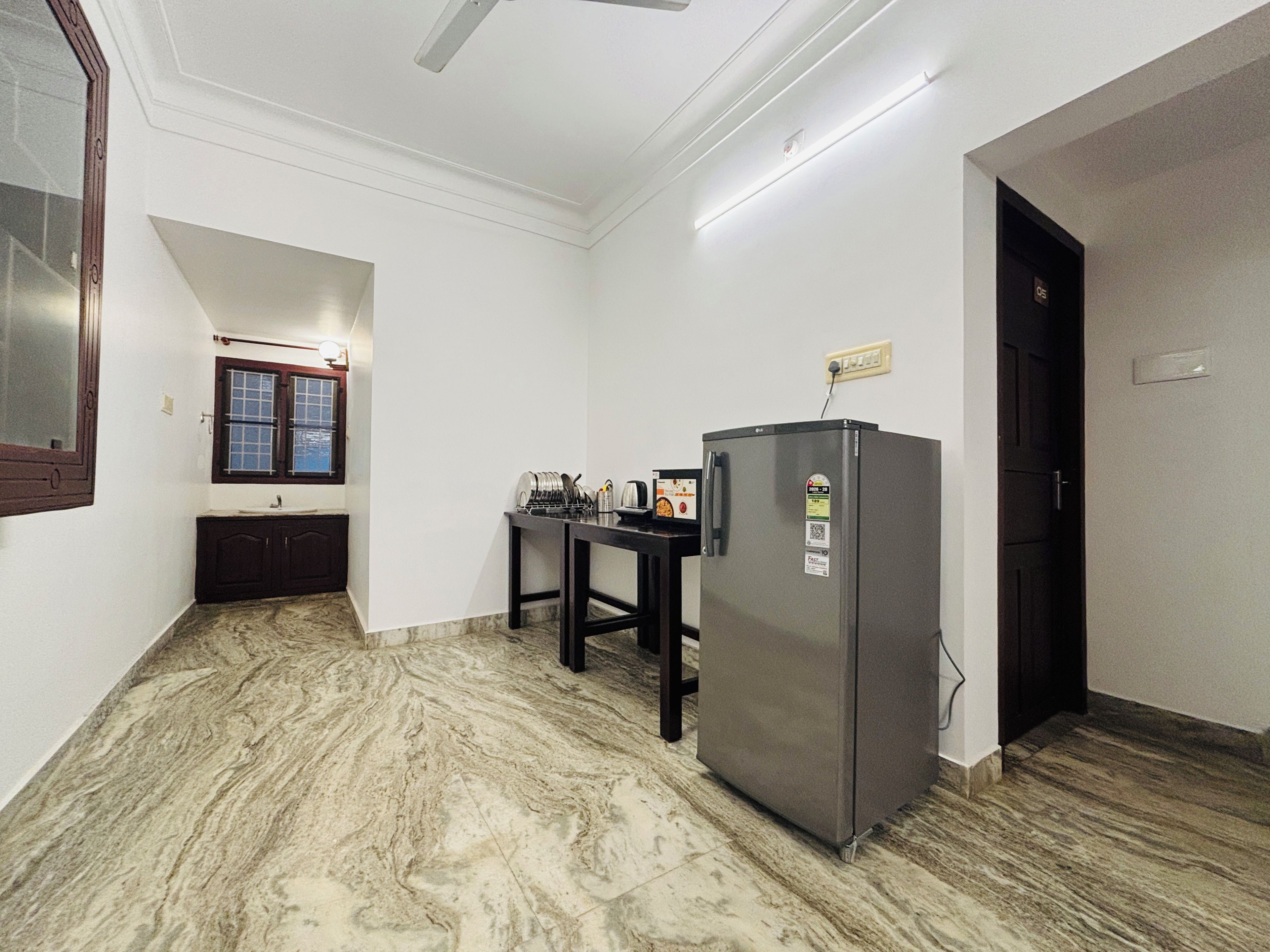 A compact kitchen with a refrigerator, a sink, and a window with wooden shutters.
