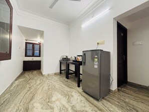 A compact kitchen with a refrigerator, a sink, and a window with wooden shutters. - Fort Grande ONE (Kochi)