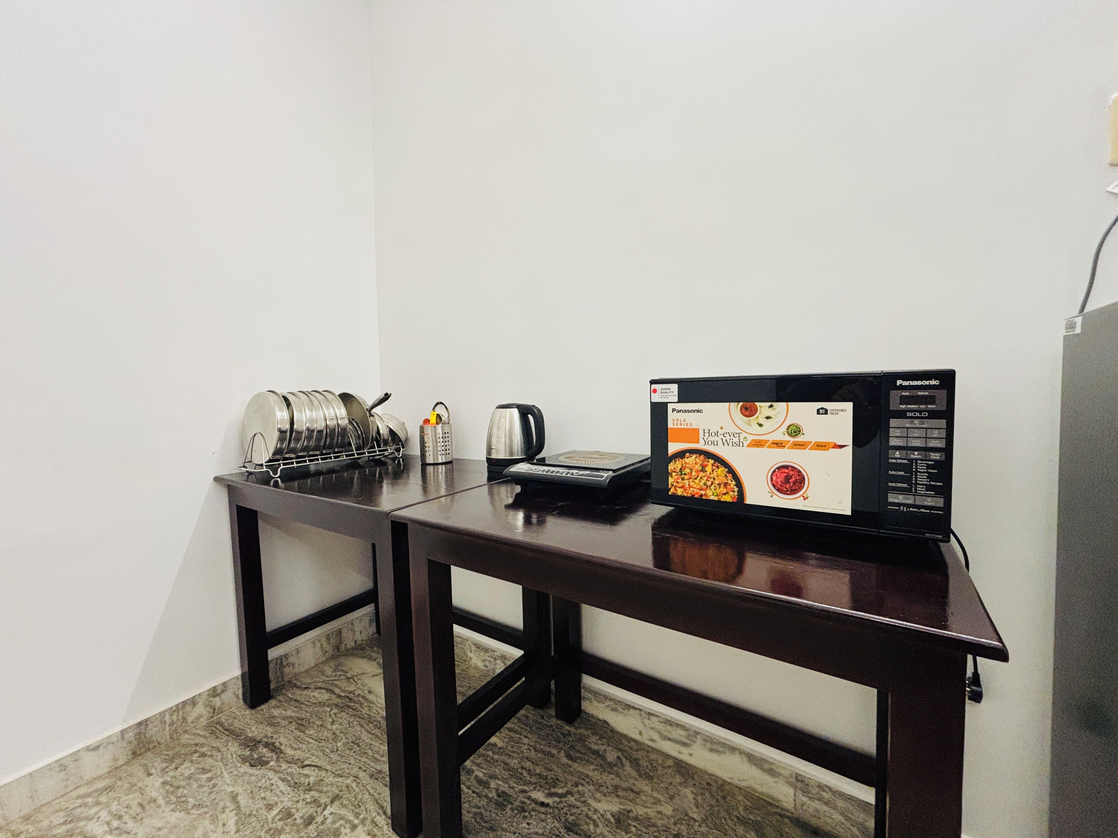 A compact kitchen area with a microwave, a kettle, and a dish rack.