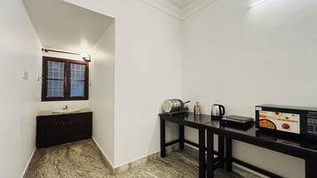 A compact kitchen with a marble floor, a sink, a window with a wooden frame, and a table with a kettle and a box of hot water tea.