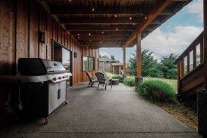 A covered patio with a barbecue grill, outdoor seating, and a view of the surrounding landscape. - Cabin Retreat w/Sauna & Cold Plunge (Salt Spring Island)