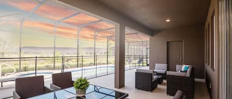 Varanda espaçosa com estrutura de vidro, móveis de exterior e vista para uma piscina.