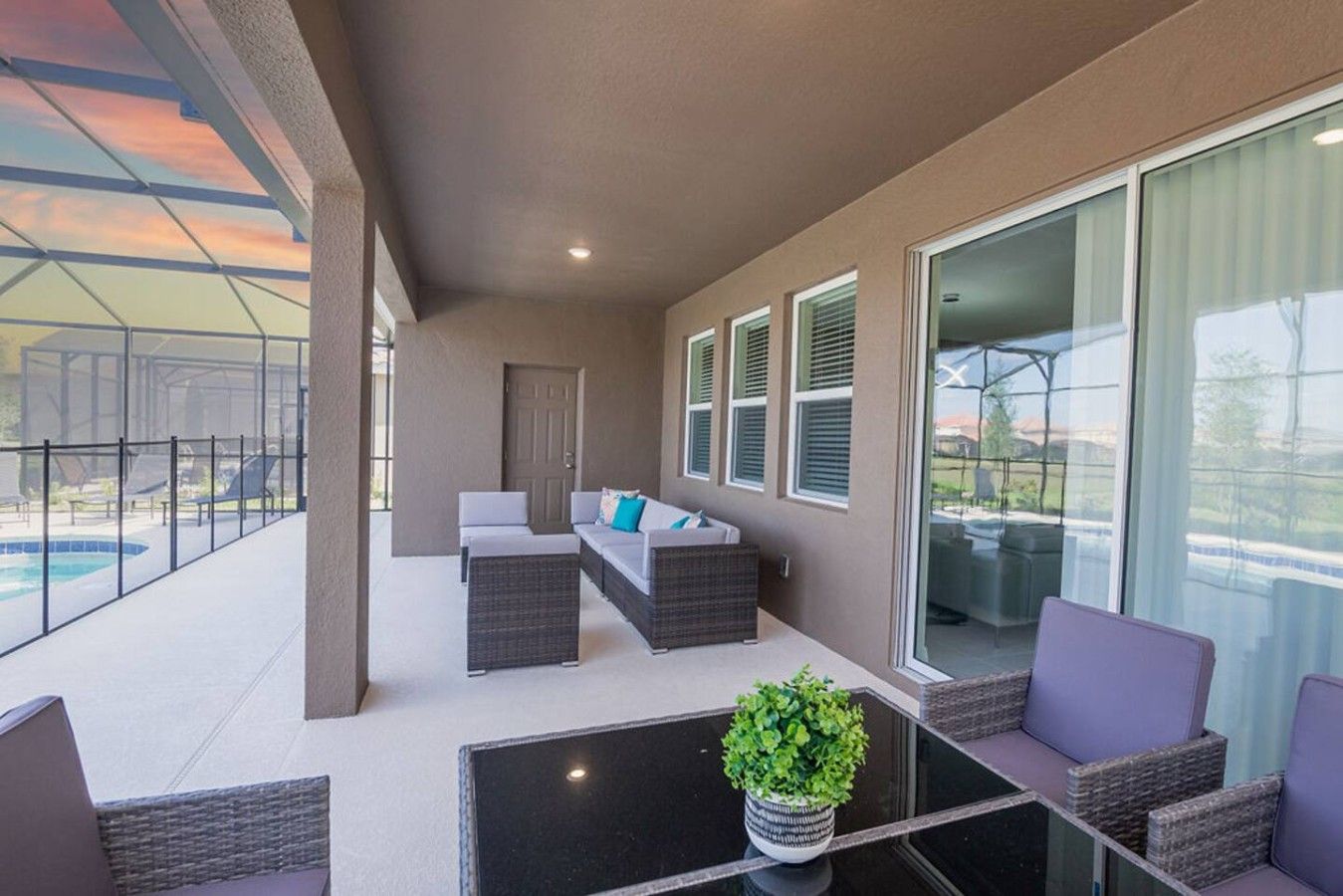 A covered outdoor seating area with a pool, wicker furniture, and a potted plant.