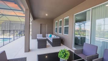 A covered outdoor seating area with a pool, wicker furniture, and a potted plant.