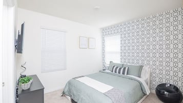 A bedroom with a bed, a desk, a chair, and a potted plant.