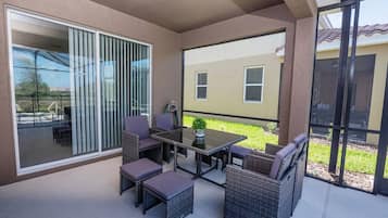 A covered patio area with a table and chairs, a sliding glass door, and a view of a building in the background.