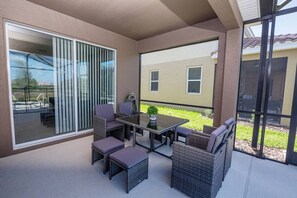A covered patio area with a table and chairs, a sliding glass door, and a view of a building in the background. - 5BR Pool Home | Mickey & Star Wars Rooms (Davenport)