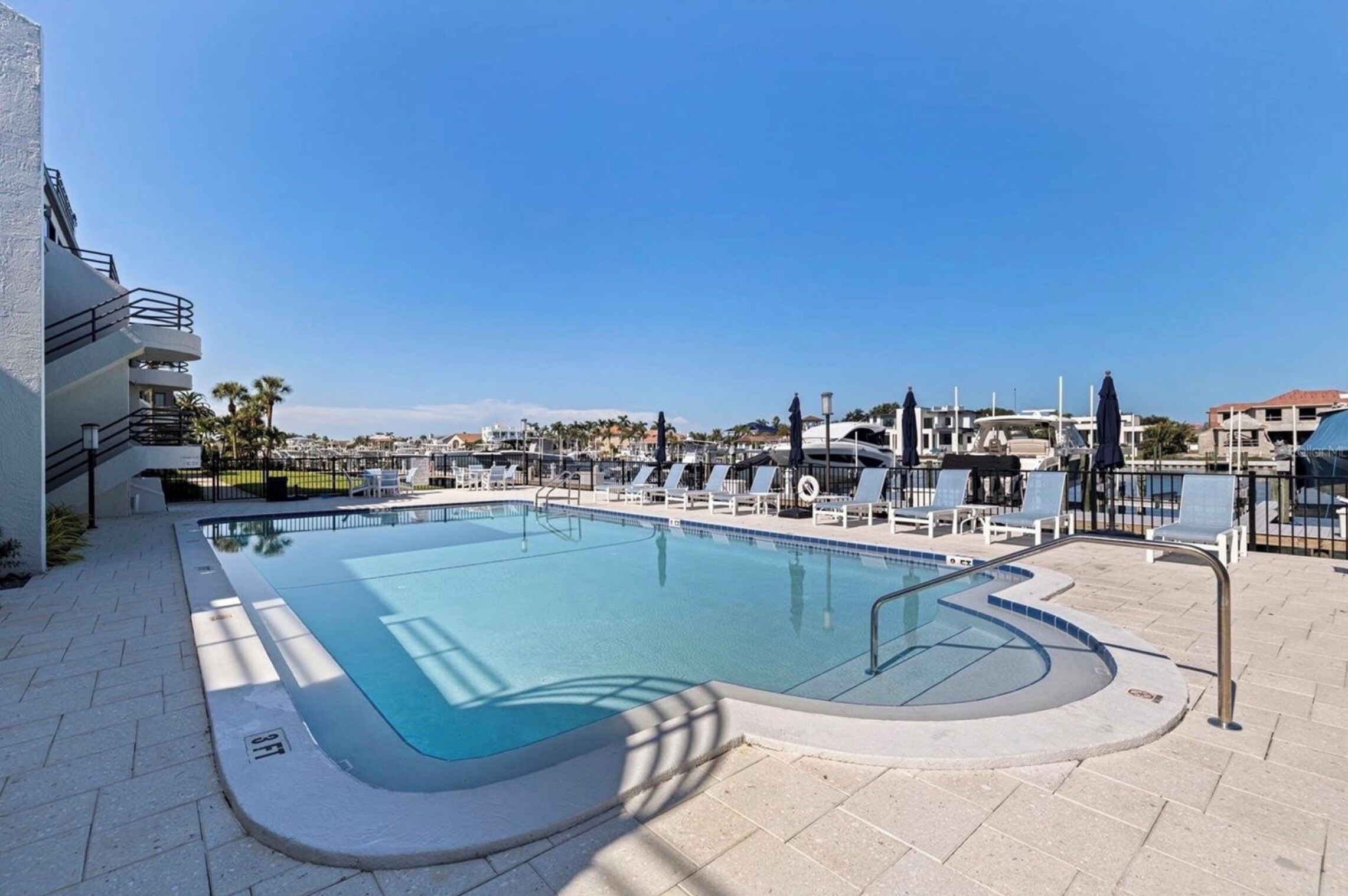 A swimming pool with a clear blue water, surrounded by lounge chairs and a fence.