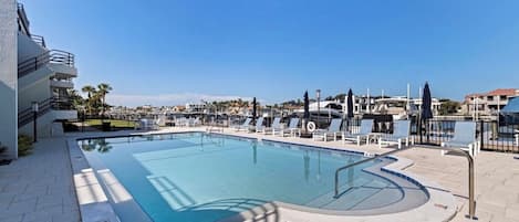 A swimming pool with a clear blue water, surrounded by lounge chairs and a fence.