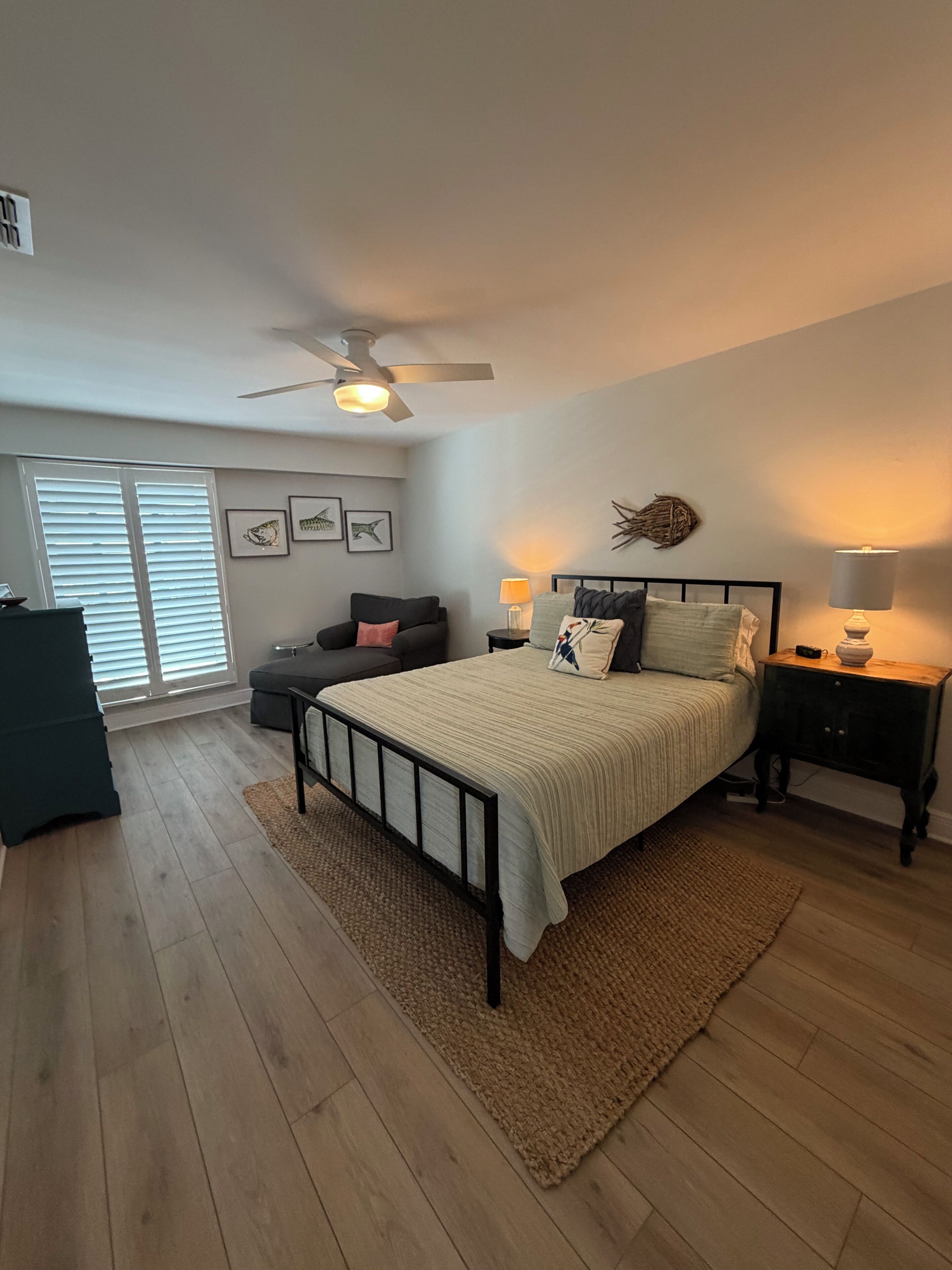 Un dormitorio con cama, mesitas de noche, ventilador de techo y ventana con persianas.