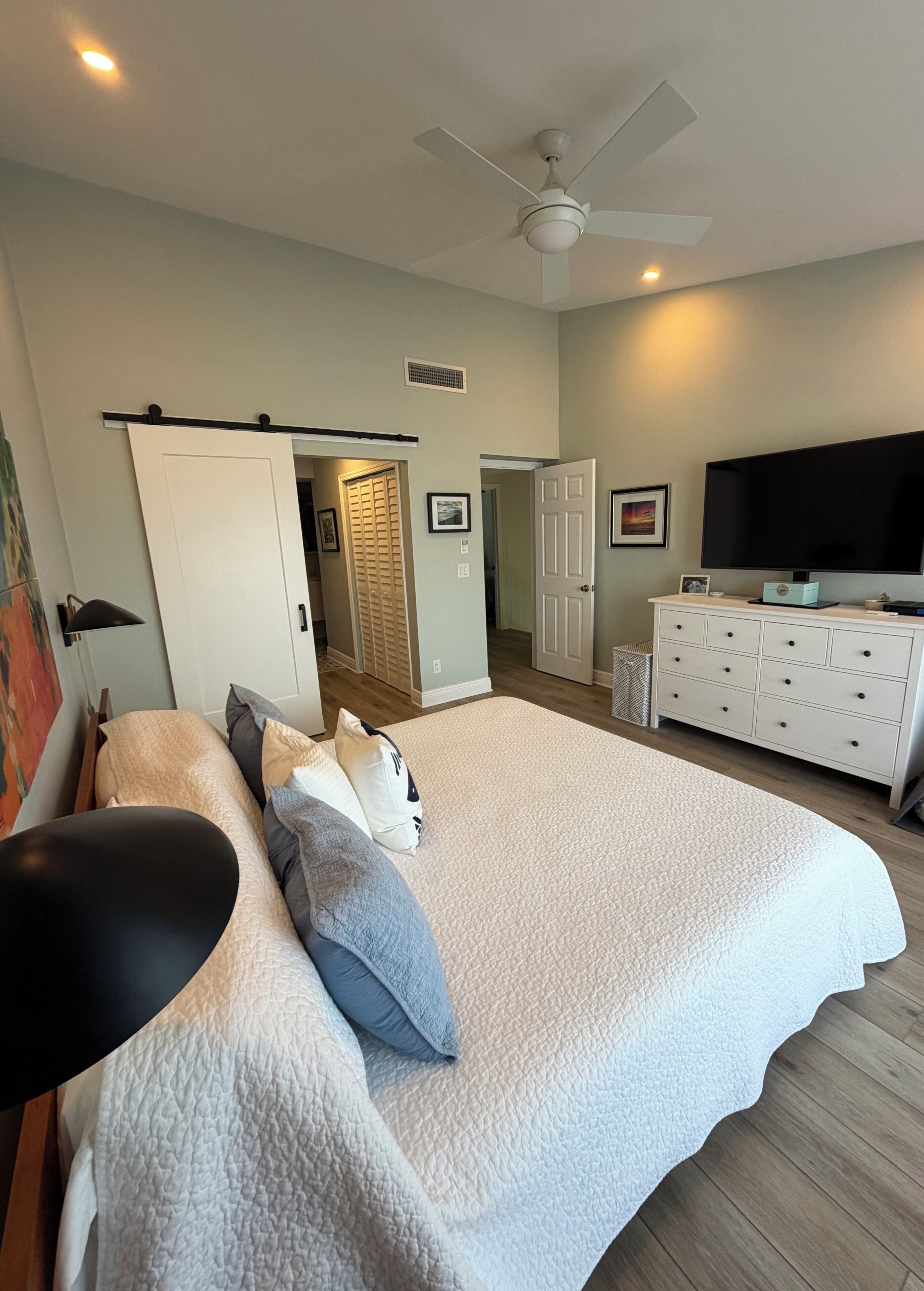 A bedroom with a bed, a dresser, a television, and a ceiling fan.