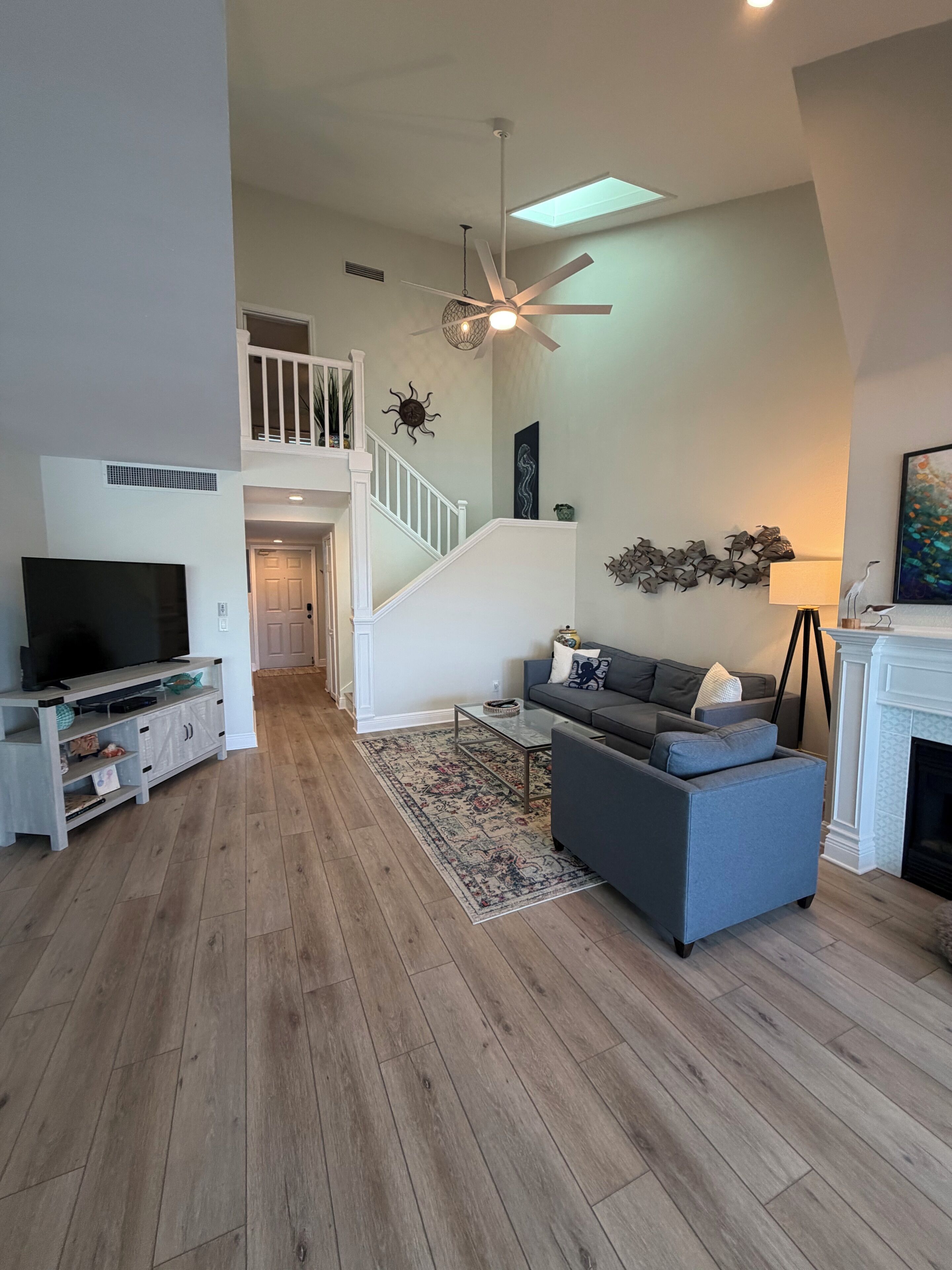 A spacious living room with a grey sofa, a flat-screen TV, and a fireplace.