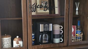 Un meuble en bois doté de plusieurs étagères et de tiroirs, contenant divers objets tels que des tasses, une machine à café et des objets décoratifs.