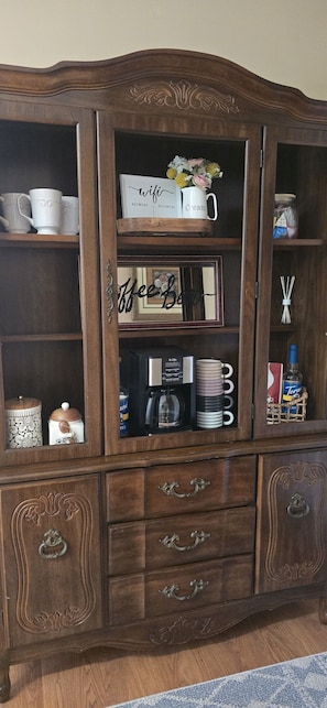Een houten kast met meerdere planken en lades, gevuld met diverse spullen zoals mokken, een koffiezetapparaat en decoratieve objecten.
