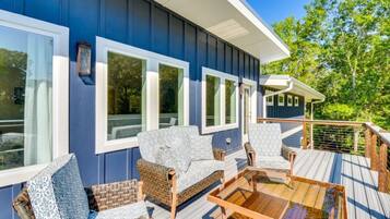 A deck with wicker furniture and a glass table, overlooking a body of water.
