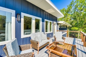 A deck with wicker furniture and a glass table, overlooking a body of water.