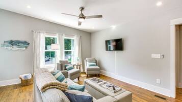 A living room with a sofa set, two armchairs, a flat-screen TV mounted on the wall, and a ceiling fan.