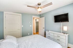 A bedroom with a bed, a dresser, a ceiling fan, and a television on the wall.