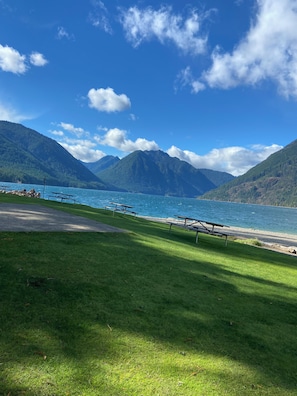 A lakeside view with picnic tables and mountains in the background.