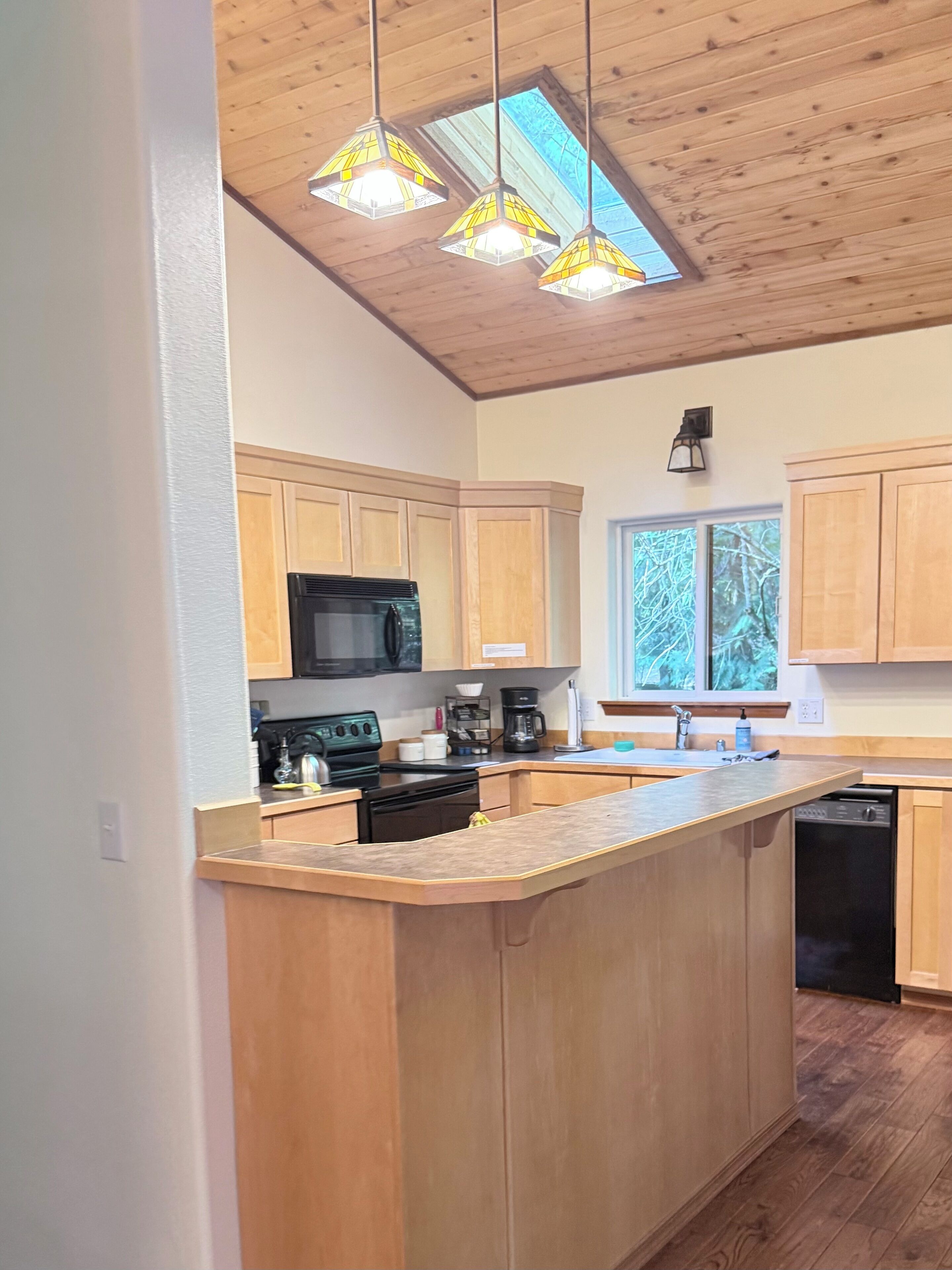 A modern kitchen with wooden cabinets, a central island, a microwave, stove, coffee maker, and a dishwasher.