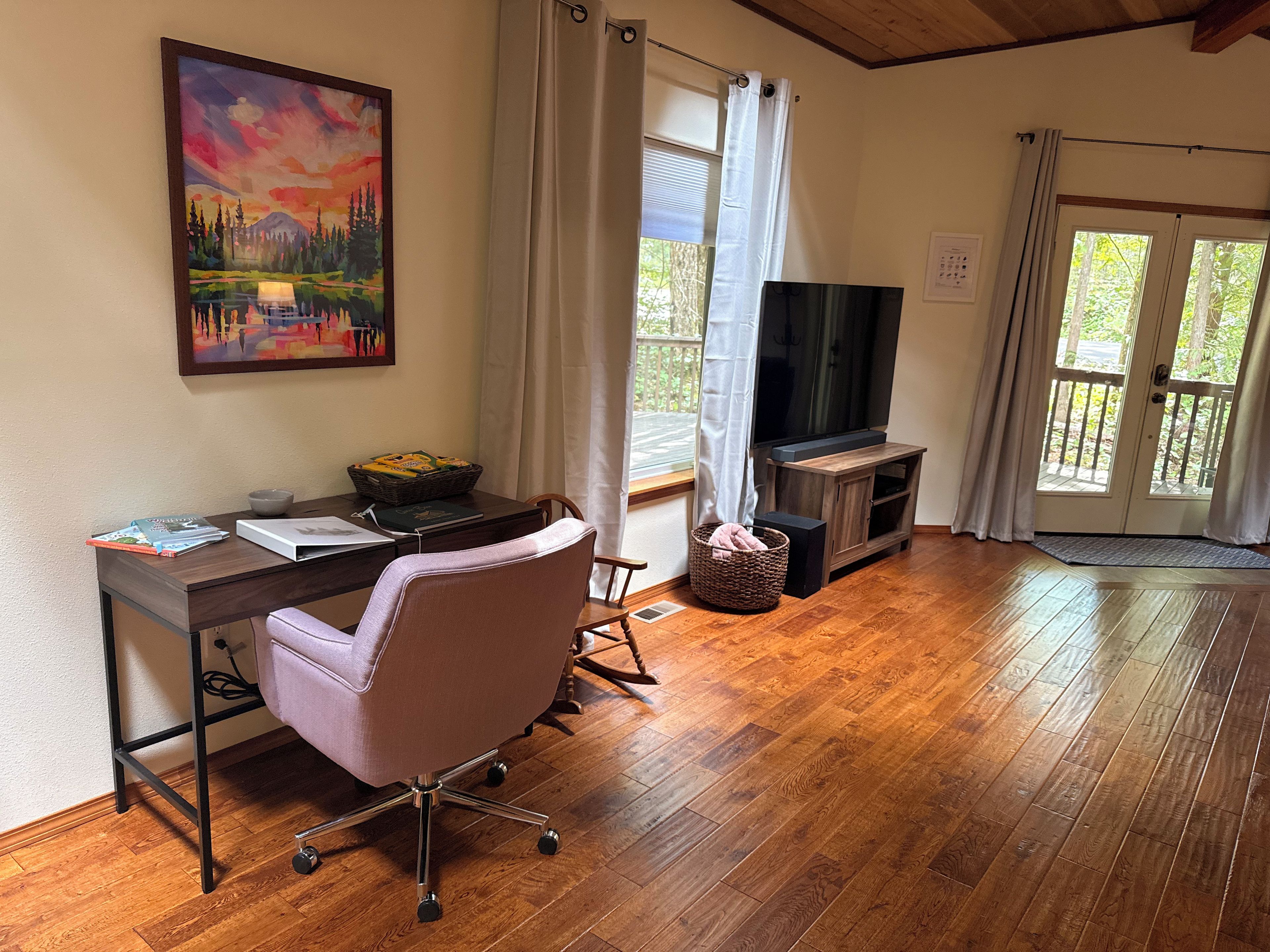 A room with a wooden desk, a chair, a television, and a painting on the wall.