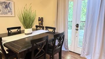 A dining area with a wooden table and chairs, a potted plant, a hanging light fixture, and a door leading to an outdoor area.