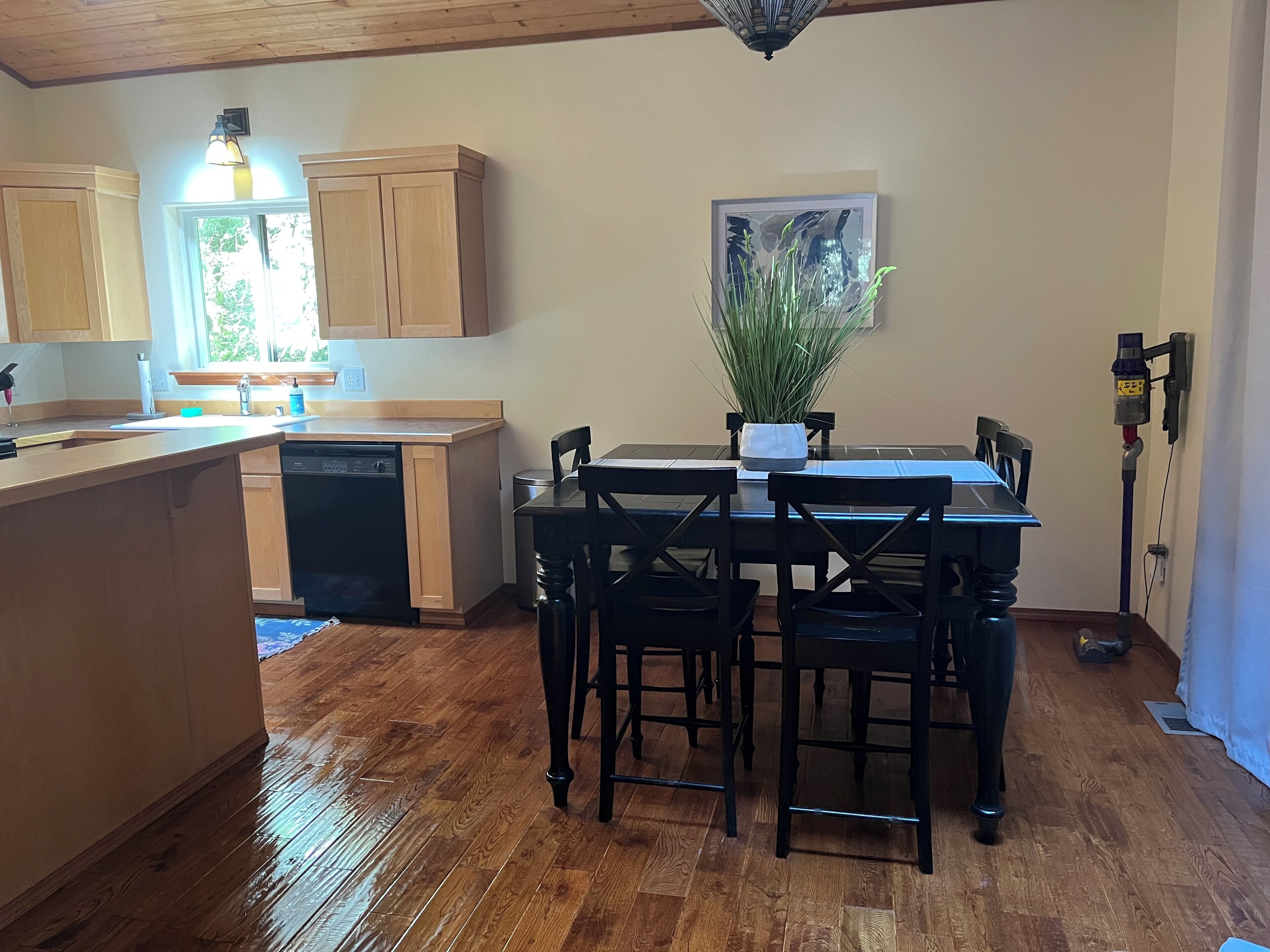 A kitchen with wooden cabinets, a dining table with chairs, a potted plant, and a ceiling light fixture.