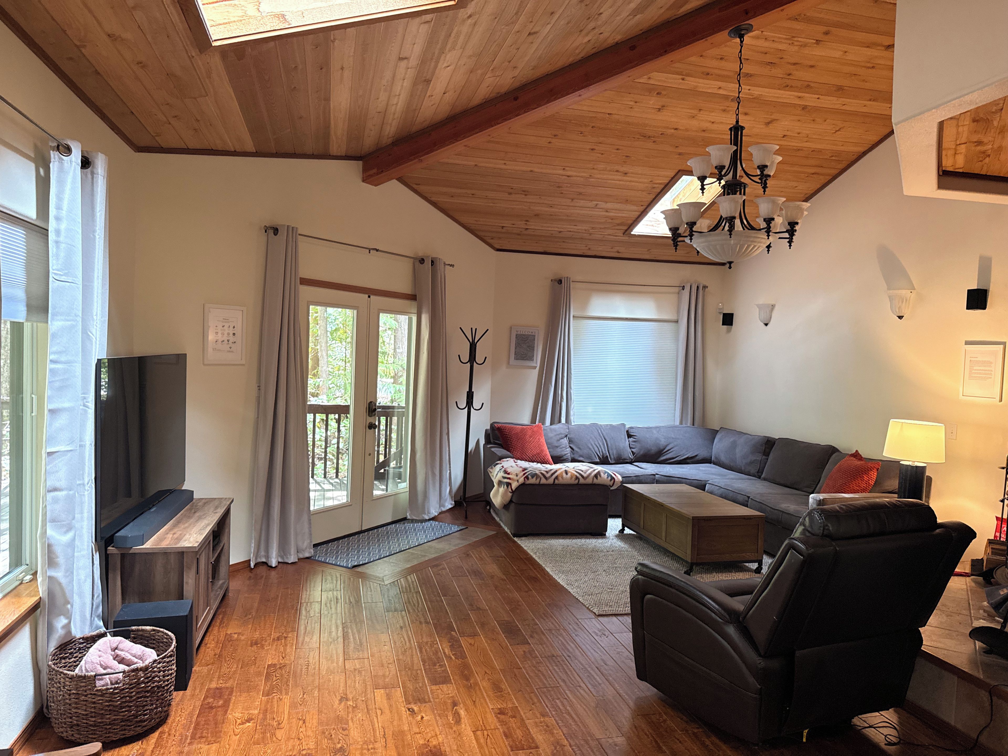 A spacious living room with a wooden ceiling, a large sofa, a television, and a fireplace.