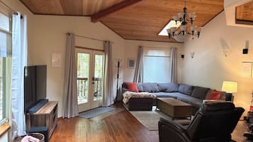 A spacious living room with a wooden ceiling, a large sofa, a television, and a fireplace.
