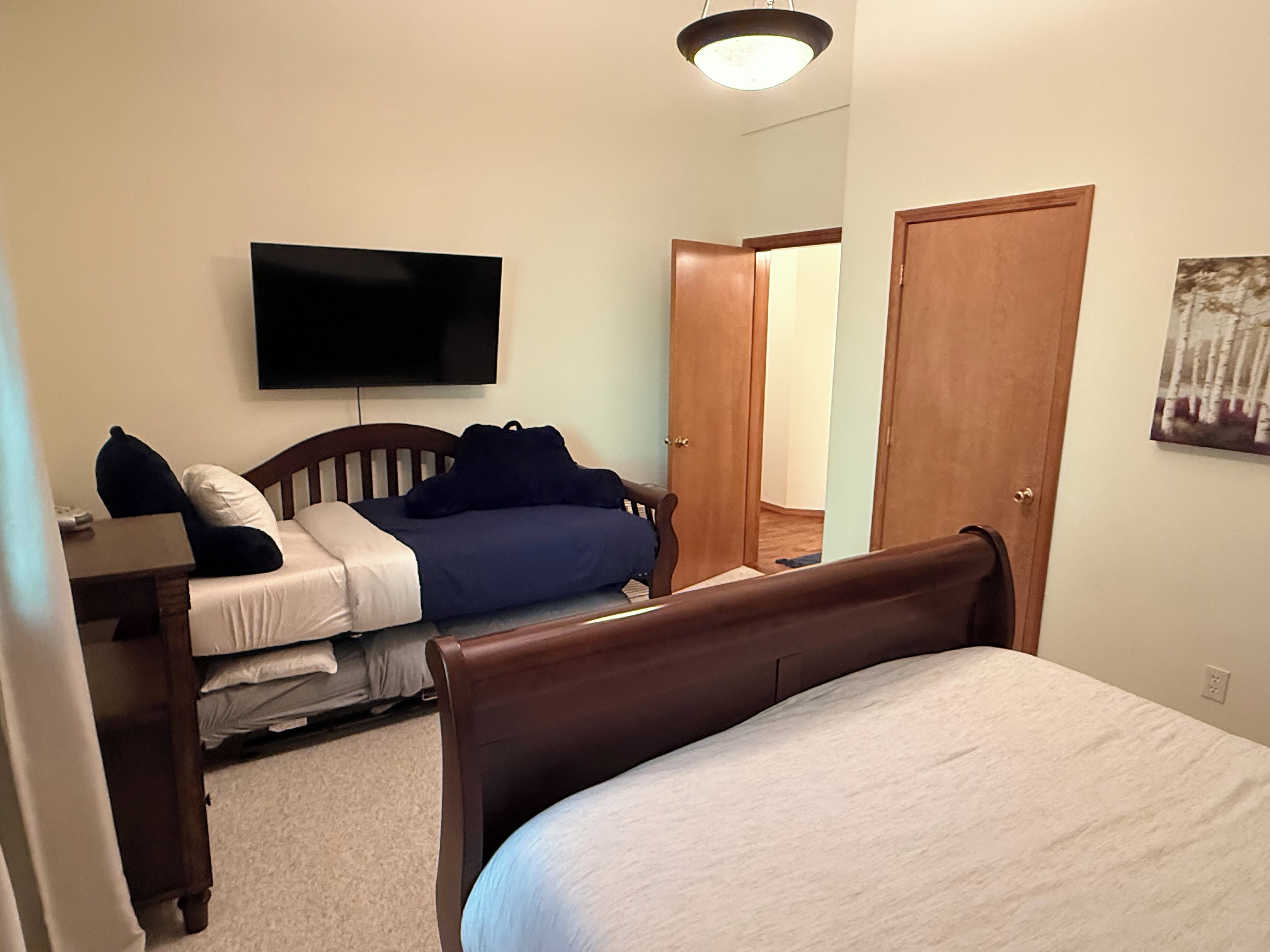 Une chambre à coucher comprenant un lit, un bureau, une télévision et une porte donnant sur une autre pièce.